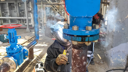 professional welder cooks the horizontal joint of the pipeline of the enterprise plant dn150 under the gate valve