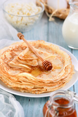 Homemade thin crepe (pancakes) with honey stacked in a stack, on a table with a pot of milk, a bowl of cottage cheese and eggs in a basket. Country style food. Traditional Slavonian, pagan holiday  