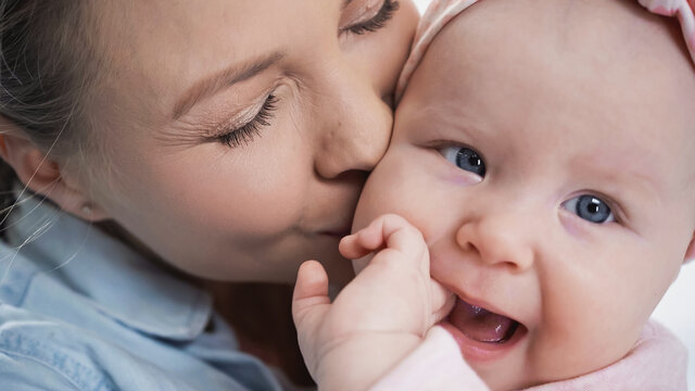 close up of mother kissing infant daughter sucking fingers.