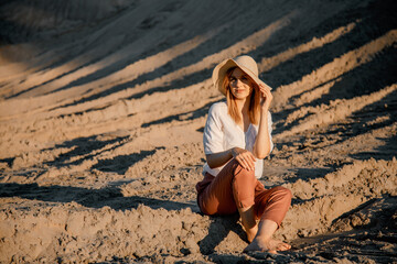Fototapeta na wymiar Young beautiful lonely woman with long hair with straw hat. A lonely girl goes down the sand dunes. Summer fashion poartrait outdoor.