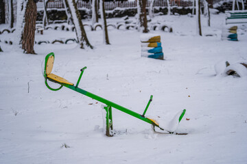 Baby swings at a playground blanketed with clean snow on a winter day in the city park