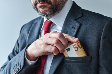 Businessman putting euro cash money into his suit pocket - obrazy, fototapety, plakaty