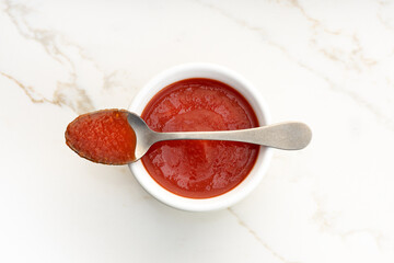 Fresh tomato sauce on bowl and spoon on white marble table