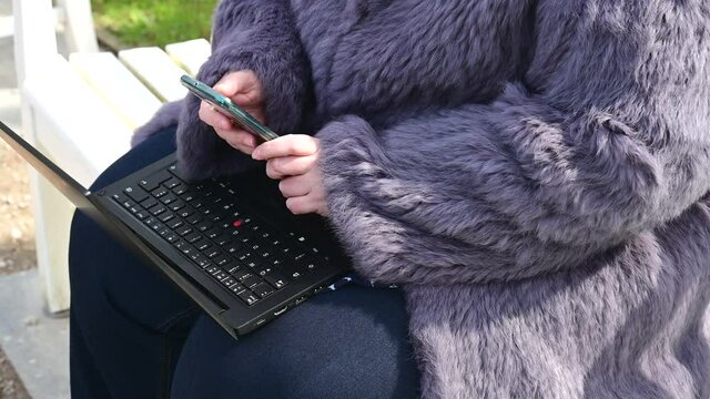 Frau in einer Kaninchenfell Jacke arbeitet im Garten mit einem Notebook im Homeoffice  