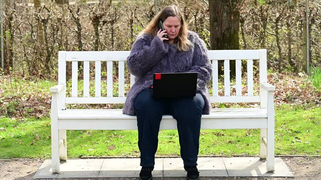 Frau in einer Kaninchenfell Jacke arbeitet im Garten mit einem Notebook im Homeoffice  