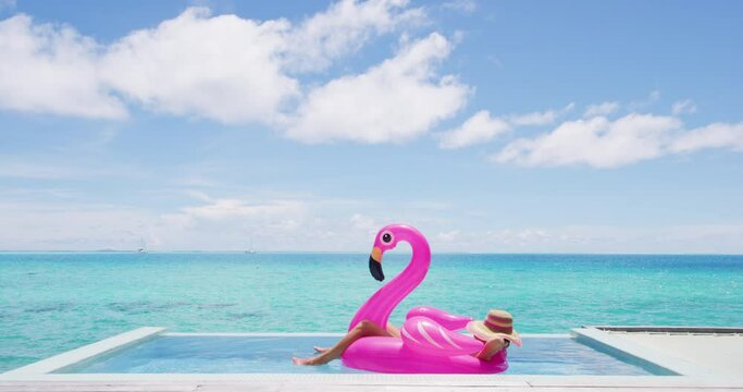 Travel vacation holidays concept. Woman in pool by beach sunbathing in bikini in inflatable pink flamingo toy mattress float in. Girl relaxing enjoying luxury lifestyle at resort pool.