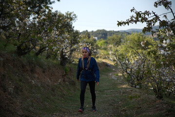 Woman in sportswear and backpack walking through a cherry bush plantation.