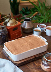 Tiramisu and coffee on a wooden background. In the background are home plants.