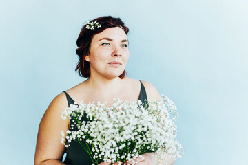 Gorgeous young freckled plus size woman with flowers in her hair holding a bouquet of gypsophila.