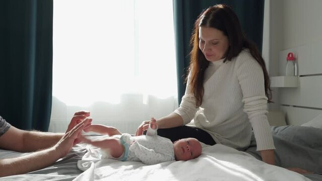 Happy family at home, mother and father with their baby on the bed in the bedroom touch baby boy for relax and feel safe, 1 month old newborn in sunlight. High quality 4k footage