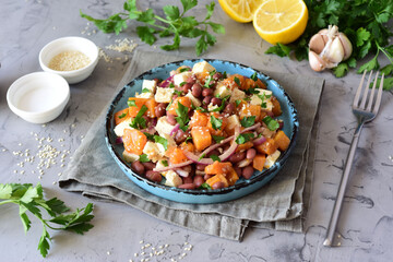 Vegetarian breakfast: pumpkin, bean and feta salad on a beautiful plate on a gray background
