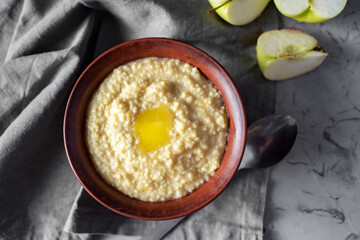 Delicious breakfast: milk porridge with butter in a clay plate. Millet porridge in a brown bowl on a gray background