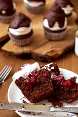 Chocolate cupcakes with cherries, cream and chocolate icing. Side view. Wooden background.