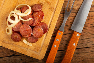 Sliced ​​calabrese sausage with onion on wooden background.