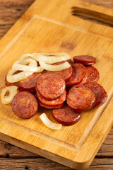 Sliced ​​calabrese sausage with onion on wooden background.