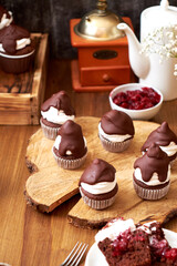 Chocolate cupcakes with cherries, cream and chocolate icing. Side view. Wooden background.