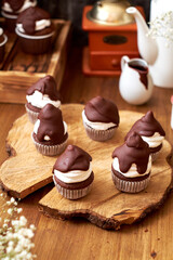 Chocolate cupcakes with cherries, cream and chocolate icing. Side view. Wooden background.