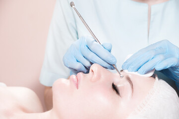 close-up, young beautiful caucasian woman lies in the salon, beautician makes cosmetic procedures with a tool in gloves