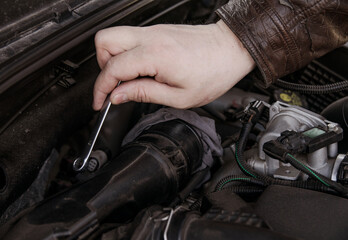 Fototapeta na wymiar A man unscrews the nuts at the EGR valve in the hood of the car with a screwdriver