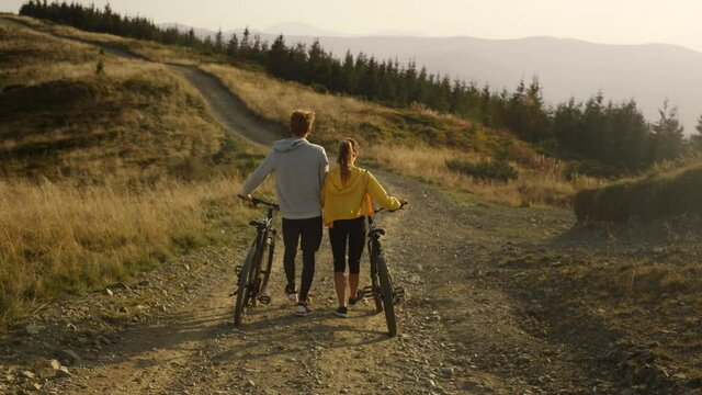 Woman and man with bikes walking on road. Couple taking break after cycling 