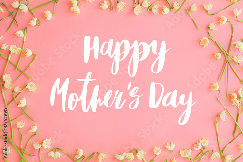 Happy mother's day. Happy mother's day text and spring flowers frame flat lay on pink paper. Stylish floral greeting card. Handwritten lettering on white spring snowflakes on pink. Mothers day