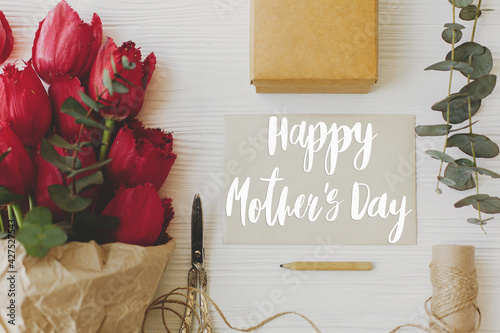 Happy mother's day. Happy mother's day text on card and red tulips, gift, pencil, scissors and twine on rustic white wood, flat lay. Stylish floral greeting card. Handwritten lettering. Mothers day