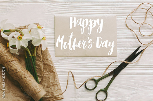 Happy mother's day. Happy mother's day text on card and daffodils, scissors, twine on white rustic wood flat lay. Stylish floral greeting card. Handwritten lettering. Mothers day