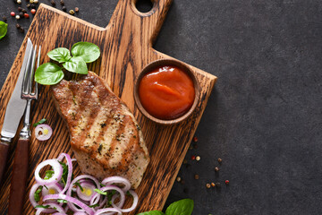 Grilled beef steak with onions and tomato sauce on a wooden board. Fried meat.