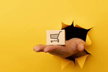 Hand with a delivery box through a yellow paper hole. Delivery concept