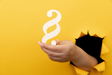 Female hand holds a paragraph as a sign of justice and law through a yellow paper hole
