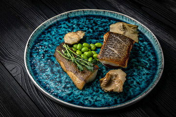 Fish grilled, on a plate, on a dark wooden table
