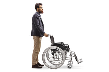 Fototapeta na wymiar Full length profile shot of a bearded man pushing an empty wheelchair