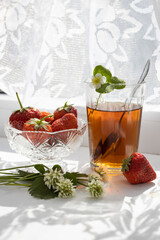Cup of tea and wild strawberries on a white lace background