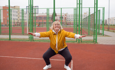 an elderly woman in a yellow jacket is doing sports exercises on a red treadmill. the stadium is a healthy lifestyle. retired people and sports.