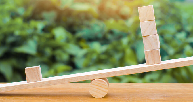 One wooden block on the scales outweighs the other four. Inequality concept. One against the others. Leadership and uniqueness. Unique, dissenting opinion, individual and standing out from the crowd