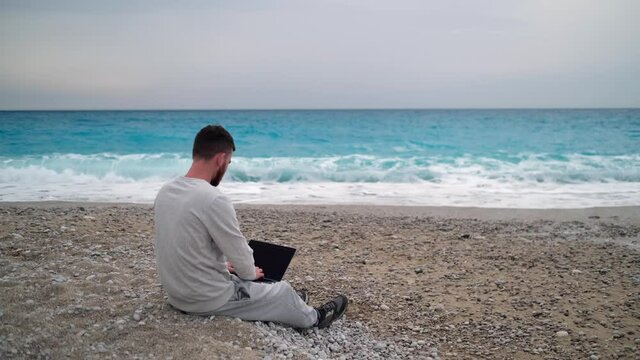 Remote Work Concept - Young Man Working On Laptop At Beach