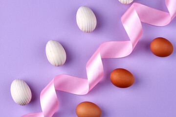 Obraz na płótnie Canvas Boiled chicken eggs and swirled pink tape isolated on purple background.