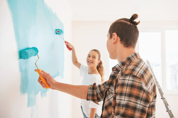 Happy young couple coloring new apartment and paint walls in blue color.