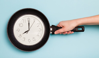 food Time. Time to eat concept. Clock face in a frying pan showing 8 a.m. on blue background. Breakfast time. frying pan in woman's hand on blue background. Woman holding a pan in a hand. Diet concept