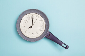food Time. Time to eat concept. Clock face in a frying pan showing 8 a.m. on blue background. Breakfast time. frying pan on blue background. Diet concept