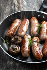 Delicious pork sausages in a frying pan on rustic wooden table