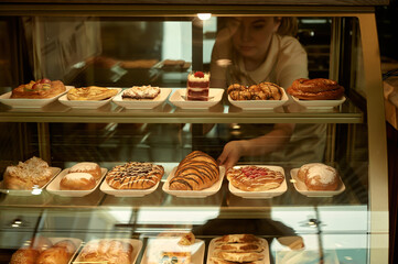 A waiter serves a customer in a pastry shop. A woman buys a cake and cookies for breakfast. 