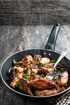 Roasted chicken wings in skillet on wooden table