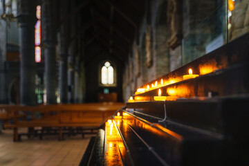 Selective focus on votive lit candle with bright soft glow and blurred background of interior of St. Marys Cathedral in Killarney, Kerry, Ireland - obrazy, fototapety, plakaty