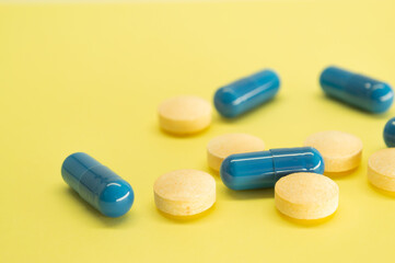 Orange pills and blue capsules on a yellow background with space for text. Medicine image. Healthcare.