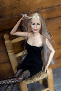 Mulhouse - France - 13 April 2021 - Portrait of blond Barbie doll wearinf ablack dress and sexy tights sitting on wooden chair on wooden background