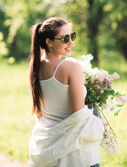 Happy smiling beautiful woman in glasses with bouquet of wildflowers walking in a summer nature