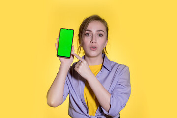 Naklejka premium Young woman pointing at green screen on smartphone on yellow background