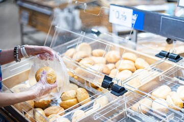 Close up woman's hand choosing bread and rolls in the grocery department of a supermarket.