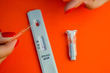 test for coronavirus on an orange background. on a matte background a sensitive strip, a girl with a bright red manicure drips onto a drop of blood for a test